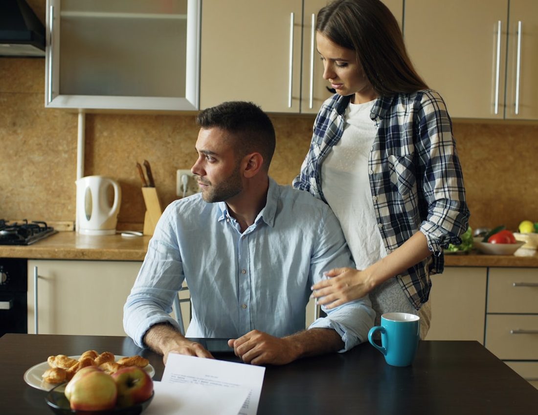 Un couple souriant à la table de la cuisine, devant un ordinateur portable et des documents